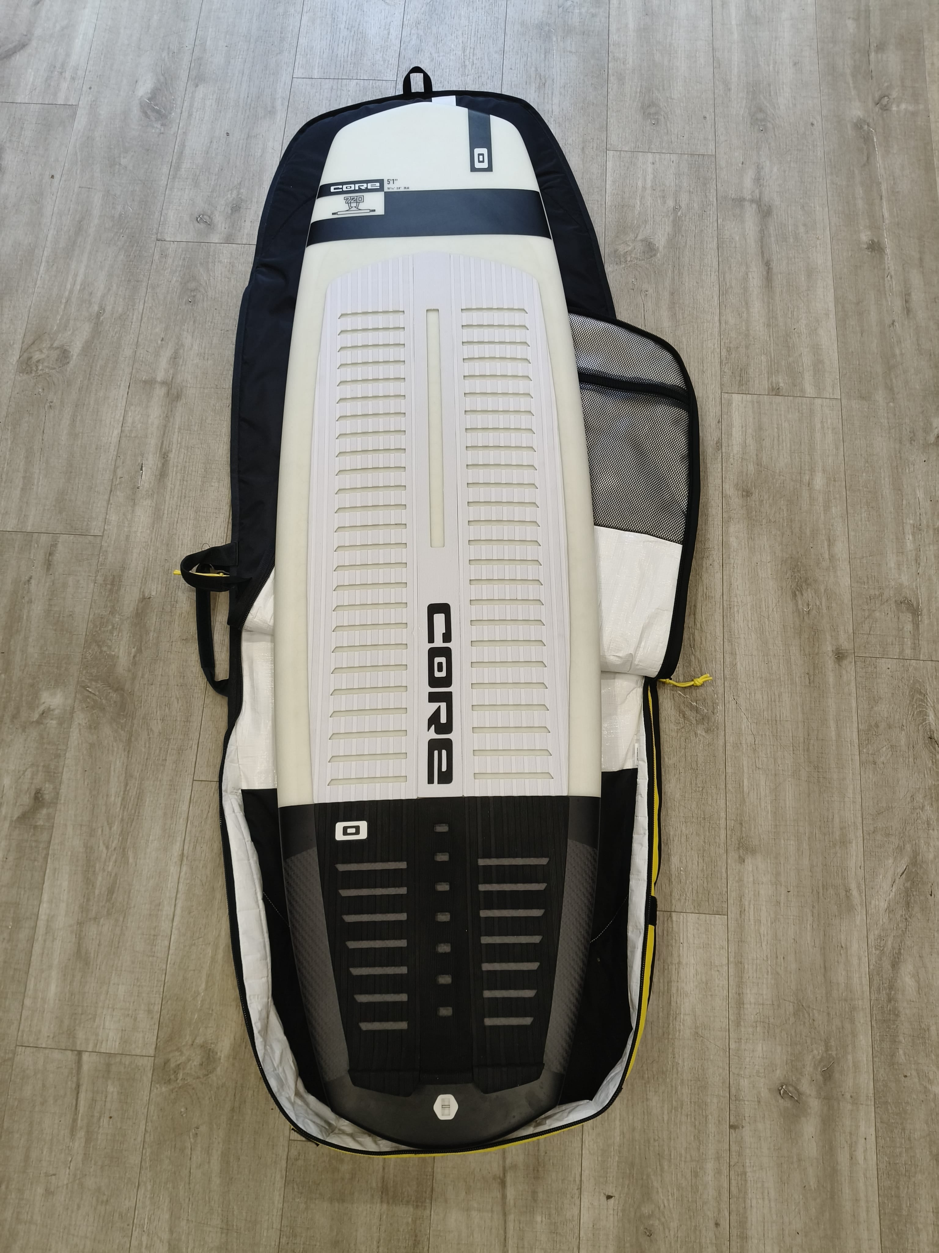 A white and black CORDA SUP board inside an open black and white carrying bag, laid flat on a light wood floor.