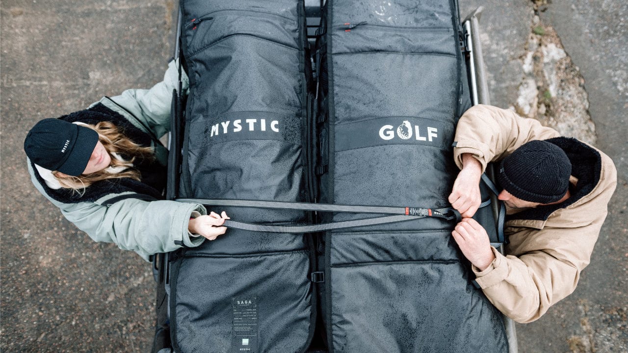 Two people securing a large black bag with 'Mystic' branding on a gray surface.