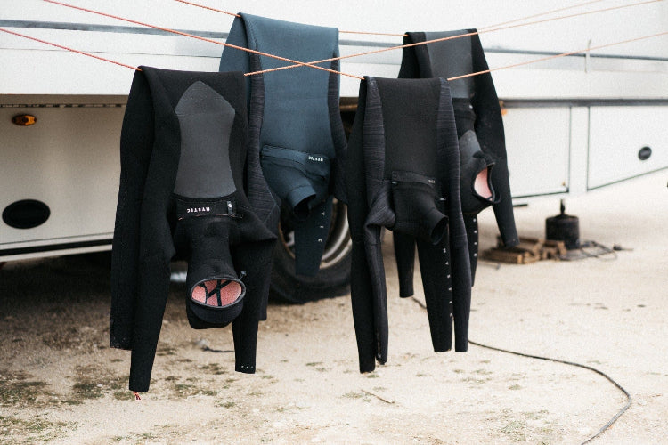 Black wetsuits hanging on a line with a trailer in the background
