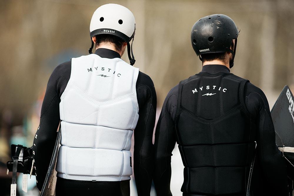 Two people wearing Mystic impact vests, wetsuits and helmets with a blurred background